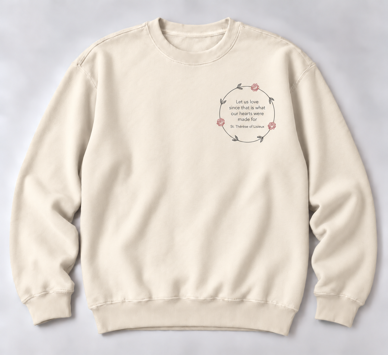 Cream crewneck sweatshirt with a small thin charcoal vine wreath, three pinkish-red roses, and the quote Let us love since that is what our hearts were made for, attributed to St. Thérèse of Lisieux